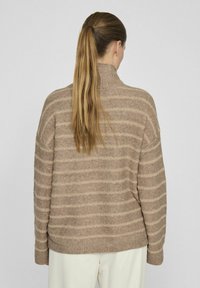 Rjav prugast pulover iz mehkega pletenega materiala z visokim ovratnikom ter rebrastimi manšeti in spodnjim robom. Tekstura se zdi prijetna in topla.