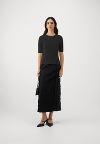 Black short-sleeve top with a fitted silhouette. Paired with a maxi skirt featuring a fringed hemline and side accents. Black heels complete the look.