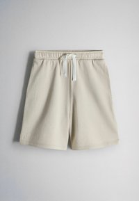 Pantalones cortos casuales beige con cintura elástica y cordón blanco, mostrados sobre un fondo gris claro.