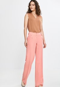 Beżowy top bez rękawów z dekoltem w kształcie litery V, w połączeniu z spodniami o wysokim stanie i szerokich nogawkach w delikatnym różu, z zapięciem na guzik i gładką teksturą.