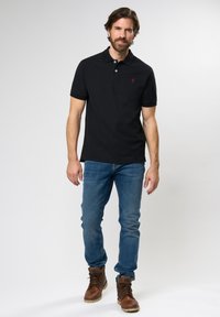 Black polo shirt made of soft fabric with a three-button placket, paired with blue jeans and brown leather boots.