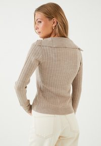 Beige ribbadtröja med krage och långärmar, med en figurnära passform. Styld med ljusa byxor.