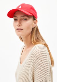 Red cotton cap featuring a white logo on the front. Styled with a rounded brim and adjustable strap at the back.