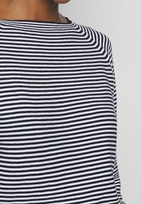 Haut à manches courtes rayé noir et blanc avec un col rond, présentant des lignes horizontales régulièrement espacées et un tissu doux et texturé.