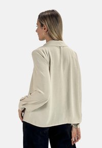 Blusa beige a maniche lunghe con un tessuto strutturato e un colletto, caratterizzata da una vestibilità comoda e maniche con polsino.