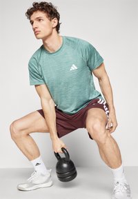 Turquoise athletic shirt with short sleeves, maroon shorts, and white accents. Person holding a black kettlebell, wearing white socks and shoes.