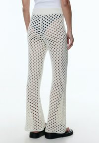 Gebreide, crèmekleurige, wijde broek met een groot open mesh patroon, voorzien van een ribgebreide tailleband en een relaxte pasvorm.