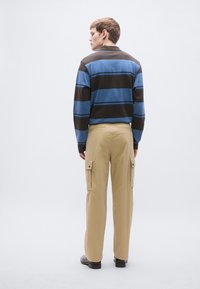 Triibuline pikkade varrukatega sinine ja pruun polo, kraega; kombineeritud tan värvi taskutega ning läbilõikeliste kinnitusdetailidega kandurpükstega.