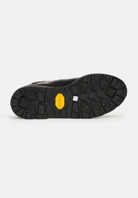 Suola nera della scarpa con scanalature profonde, un logo Vibram giallo al centro e piccole macchie arancioni incorporate nel motivo della scanalatura.