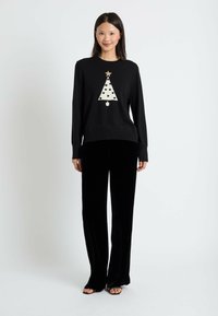 Pull noir avec un design d'arbre de Noël blanc, des pois noirs et une étoile dorée, associé à un pantalon large en velours noir.