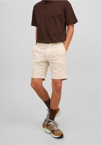 Hnědý tričko s krátkým rukávem, světle béžové kraťasy s kapsami, nošeno s hnědými kotníkovými ponožkami a vícebarevnými teniskami.