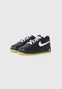 Crne kožne tenisice s bijelim vezicama i bijelim Nike logom. Teksturalni crni gornji dio, gumeni potplat boje gume i perforirani dizajn prstiju.