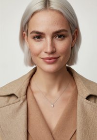 Sølvkæde med dråbeformet vedh�æng, båret med en beige tekstureret blazer og top, med en blød, neutral farvepalet.