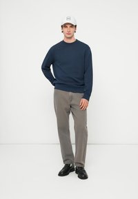 Tmavomodrá mikina s okrúhlym výstrihom a dlhými rukávmi, vyrobená z bavlny. Kombinovaná so sivými nohavicami a čiernymi topánkami, stojaca na bielom pozadí.