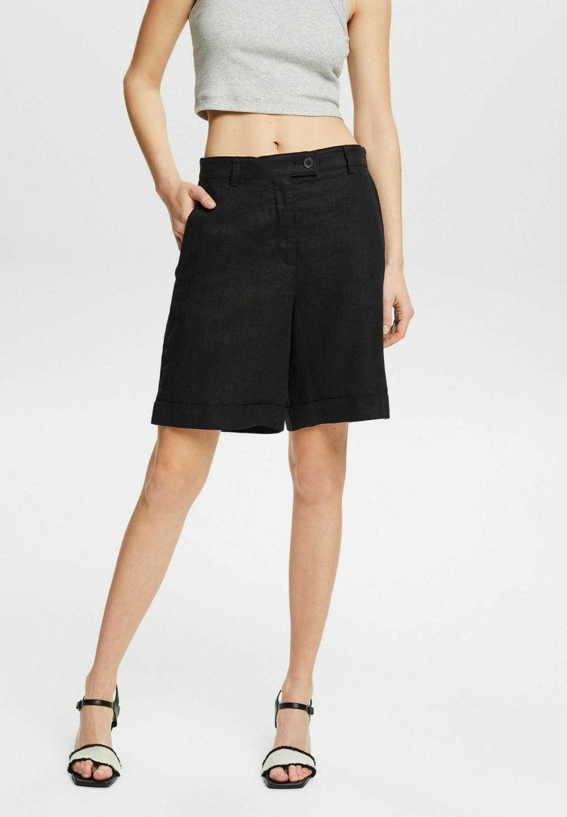Zwarte linnen shorts met een relaxte pasvorm, omgeslagen boorden en zijzakken. Gecombineerd met een grijze crop top en zwarte sandalen.