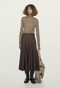 Maglione a collo alto marrone, gonna in pelle marrone scuro a vita alta, stivali al ginocchio neri, in mano un cardigan chiaro. Design minimalista.