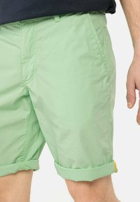 Lichtgroene shorts van een zachte, lichtgewicht stof met opgerolde mouwen en zijzakken. Kenmerkt zich door gestikte naden en een subtiele glans.
