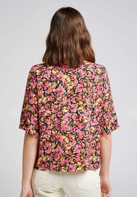 Haut fleuri en tissu noir avec des fleurs roses, orange et vert éclatantes. Manches courtes et lâches avec une coupe décontractée.