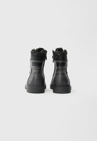 Sorte faux læder støvler med en struktureret finish, pelsforede manchetter, side lynlåse og gummisåler, med en robust hæl og minimale detaljer.