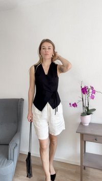 Sort ærmeløs indpakningstop med side-binding, parret med hvide shorts. Tilbehøret inkluderer en sort håndtaske og store guldringe.