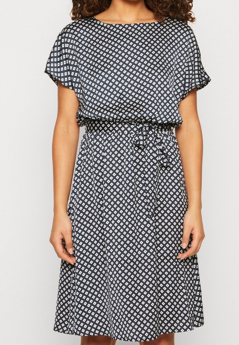 Robe à manches courtes en tissu marine avec motif géométrique blanc, taille cintrée et jupe fluide. Légère avec une texture lisse.