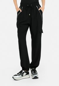 Pantalons cargo noirs avec taille élastique, fermeture à cordon de serrage, poches latérales et accents en piping blanc. Associés à des baskets à motifs.