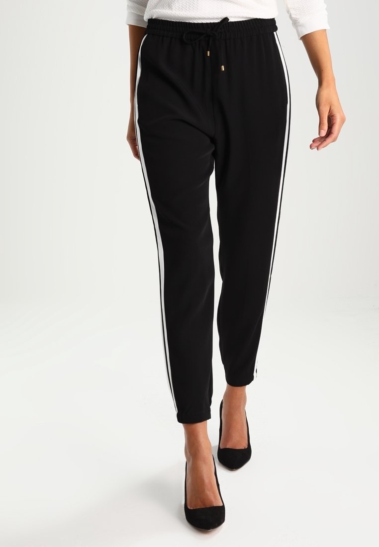 Pantalon de sport noir avec taille à cordon de serrage, présentant des bandes blanches contrastantes sur les côtés, une coupe fuselée et une texture de tissu lisse.