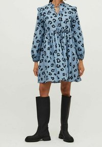 Sininen mekko mustalla leopardikuvioinnilla, frillakäsivarsilla ja avonaisella kaula-aukolla. Yhdistetty pitkien mustien saappaan kanssa. Puuvillamateriaali.