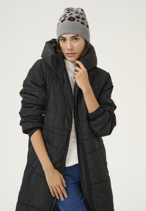 Cappotto imbottito nero con chiusura a zip e cappuccio, caratterizzato da una texture trapuntata. Abbinato a un berretto grigio decorato con punti colorati.