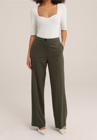 Vit ribbad bodysuit med fyrkantig halslinje, i kombination med olivgröna vida byxor. Byxorna har fickor och en framknäppning.