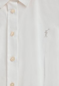 Weißes Hemd mit Knopfleiste aus glattem Stoff. Verfügt über klare Knöpfe und eine kleine graue Stickfigur auf der linken Seite.