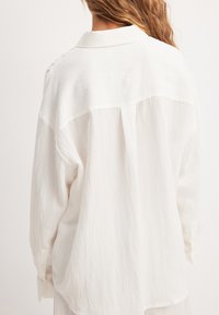 Witte, lose blouse met een gladde textuur, een zachte kraag en knoopmanchetten, met een eenvoudige rugplooidetails.