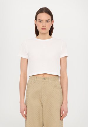 Witte crop-top in een gemêleerde stof met een ronde halslijn en korte mouwen, gecombineerd met beige broek met een patroon van kleine stippen.