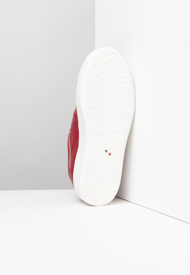 Sneaker rossa in pelle con suola in gomma bianca, caratterizzata da un motivo zigzag testurizzato per la presa e un design minimalista.