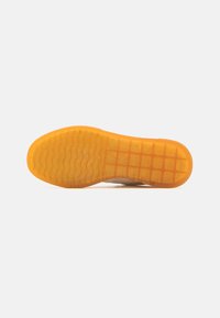 Schuhsohle aus orangefarbenem Gummi mit strukturiertem Muster, das ein Rautenmuster und geschwungene Linien zeigt, und die Langlebigkeit und die Griffigkeit der Struktur verdeutlicht.