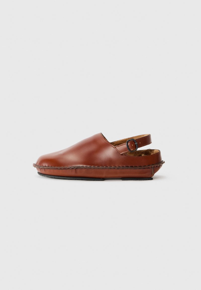 Sabots en cuir marron avec un bout arrondi, une sangle de boucle sur le côté et des coutures visibles. Doublure intérieure douce et semelle en caoutchouc plate pour le confort.