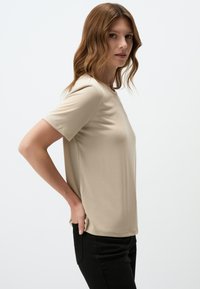 Beige t-shirt met korte mouwen in een relaxte pasvorm en een ronde halslijn. Katoenachtige textuur, soepele stof en zijsplitten voor bewegingsgemak.