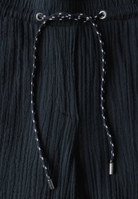 Pantaloni corti in tessuto scuro e texture con pieghe verticali, dotati di un cordoncino con un motivo intrecciato in bianco e nero e occhielli metallici argentati.