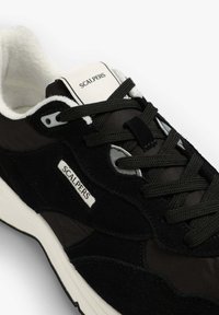 Sneakers neri realizzati in materiali scamosciati e in rete. Presentano un colletto imbottito, lacci testurizzati e un'etichetta bianca con logo sulla linguetta.