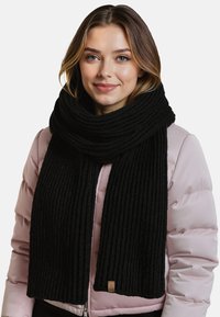 Bufanda negra de punto acanalado con una textura gruesa, colocada alrededor del cuello, combinada con una chaqueta de plumas rosa claro. Incluye una pequeña etiqueta de cuero.