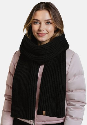 Zwarte geribbelde gebreide sjaal met een dikke textuur, rond de nek gedrapeerd, gecombineerd met een lichtroze pufferjack. Inclusief een klein leren label.