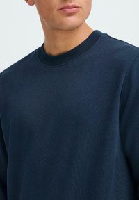 Felpa blu navy con collo a giro, realizzata in un tessuto morbido e testurizzato. Presenta polsini e colletto a coste per una maggiore durata.