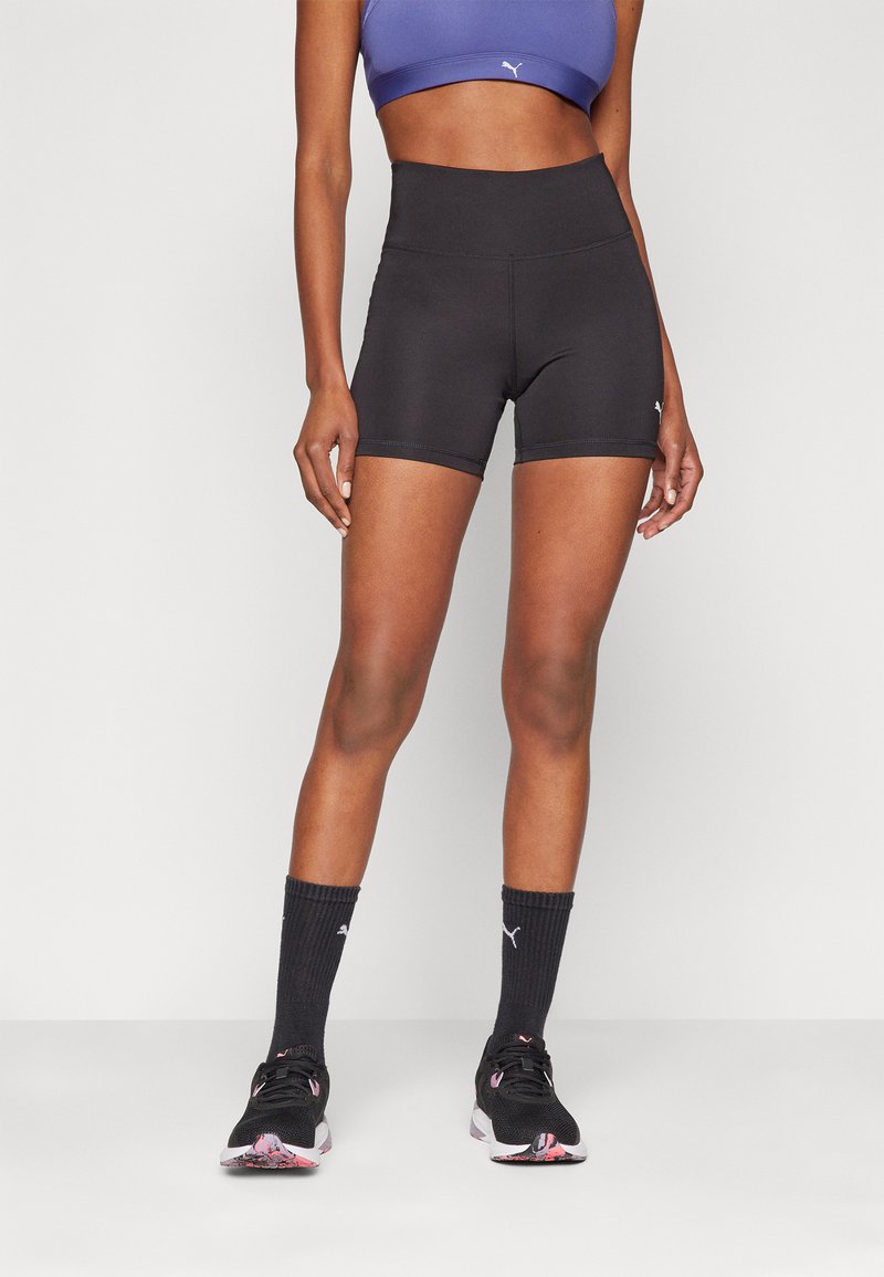 Sorte højtaljede shorts med en glat tekstur, parret med en lilla sports-bh, sorte sokker og sorte løbesko med en farverig sål.