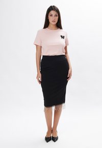 Rosa Kurzarm-T-Shirt mit schwarzem Schmetterlings-Pailletten-Detail, kombiniert mit einem schwarzen knielangen Rock mit Fransenrand und schwarzen spitzen Schuhen.