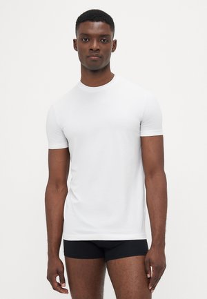 Weißes Kurzarm-T-Shirt aus weichem Stoff, mit Rundhalsausschnitt und schmalem Schnitt, kombiniert mit schwarzen eng anliegenden Shorts.