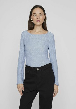 Top de manga larga azul claro con un patrón de olas texturizado y un escote amplio, combinado con pantalones negros de cintura alta.