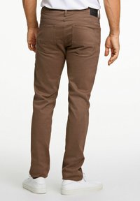 Bruine katoenen broek met een slim fit, voorzien van twee achterzakken en een zwart label op de tailleband. Gecombineerd met witte sneakers.