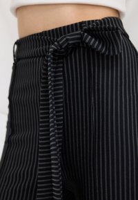 Pantalons en tissu rayé noir et blanc avec un détail de taille nouée, une texture lisse et une coupe ajustée.