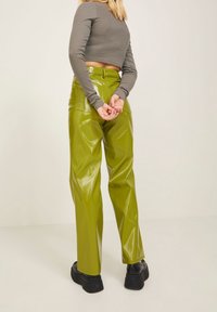 Wysokotaliwowe, błyszczące zielone spodnie z winylu o szerokich nogawkach; w połączeniu z dopasowaną szaro-skalowym bluzką z długim rękawem. Widoczne czarne buty na platformie.