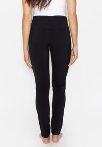 Schwarze Stretch-Jeans mit tailliertem Design, hoher Taille und Gesäßtaschen, die eine glatte Textur und klare Linien zeigen.